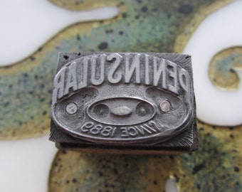 Puede incluir: Un bloque de impresión de metal vintage con el texto "DENISULAR SINCE 1889" en letras en relieve. El bloque es rectangular y tiene un borde superior ligeramente redondeado.
