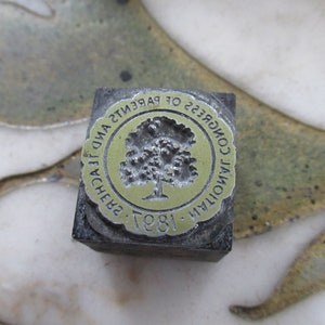 May include: A vintage metal printing block with a circular design featuring a tree and the text "NATIONAL CONGRESS OF PARENTS AND TEACHERS, 1897".