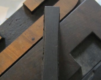 Può includere: Primo piano di un blocco di stampa tipografica in legno nero, che mostra il dettaglio della lettera 'I' incisa. Il blocco è appoggiato su un blocco di legno più grande, che è anche inciso con una lettera.