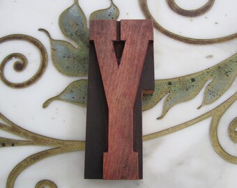 Peut inclure: Une lettre Y en bois de couleur brun foncé avec un centre brun plus clair. La lettre est sur un fond blanc avec un motif décoratif.