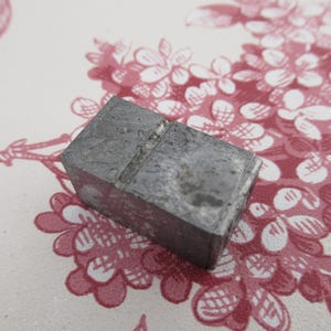 May include: A gray metal block with a groove running across the top. The block is slightly worn and has a rough texture.