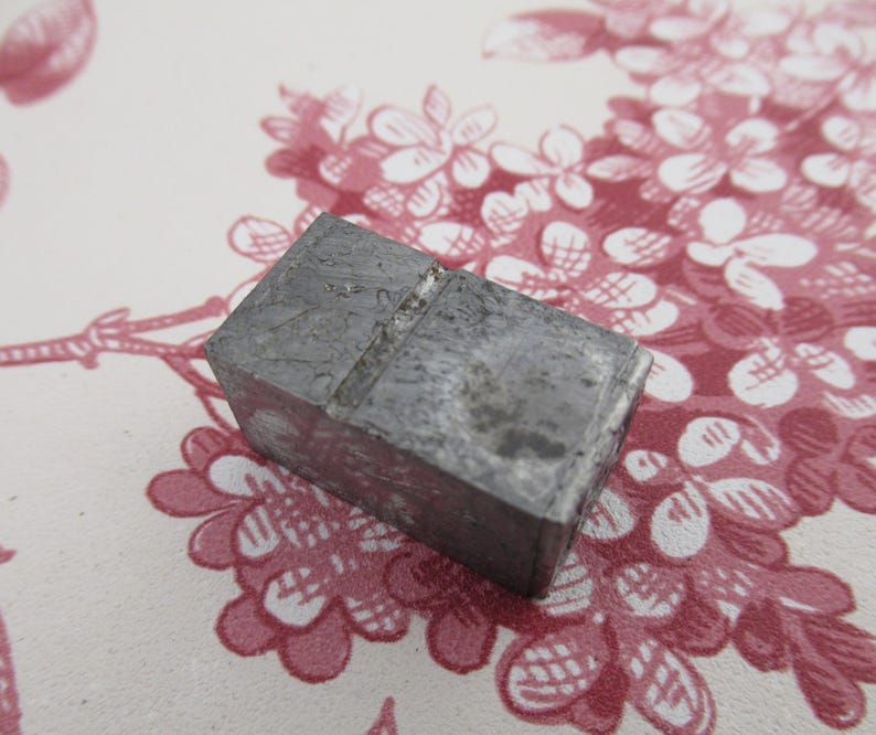 May include: A gray metal block with a groove running across the top. The block is slightly worn and has a rough texture.