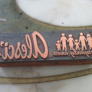 May include: A vintage printing block with the words "Everybody loves Alec's" and a copper silhouette of a family.