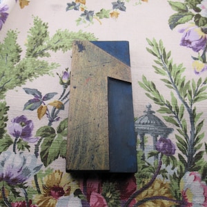 May include: A vintage wooden printing block in the shape of the number one. The block has a rectangular shape with a blue and tan color scheme. The number one is carved out of the wood, creating a negative space.