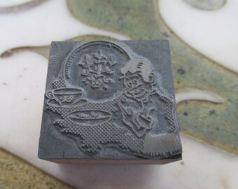 Puede incluir: Un bloque de impresión de metal vintage con un diseño de una persona sosteniendo una taza de té y un platillo. El diseño también incluye un patrón floral y un plato.