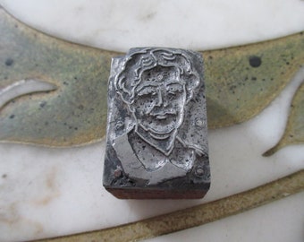 Könnte beinhalten: Ein Vintage-Metall-Druckblock mit einem detaillierten Porträt eines Mannes mit lockigem Haar und Schnurrbart. Der rechteckige Block hat einen Holzsockel und weist Gebrauchsspuren auf, die auf sein Alter und seine Verwendung im Druck hinweisen.