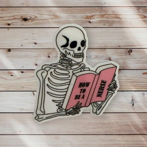 May include: A white skeleton with a crescent moon on its forehead is reading a pink book titled "How to be a Nurse".