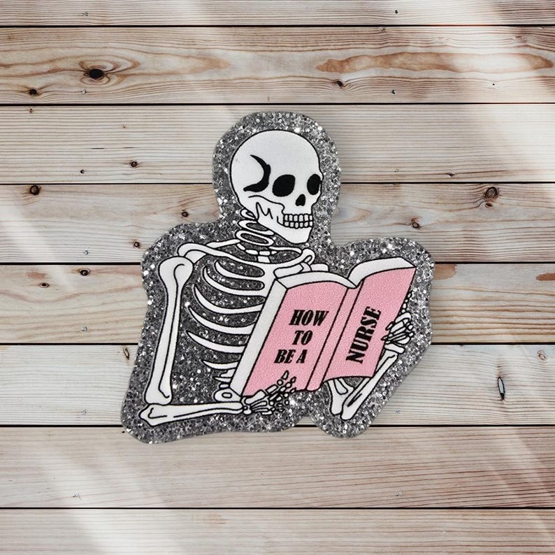 May include: A silver glitter skeleton is reading a pink book that says "How to be a Nurse".