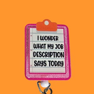 May include: Pink glitter badge holder with a white clip and a white retractable reel. The badge holder has a white background with black text that reads "I wonder what my job description says today".