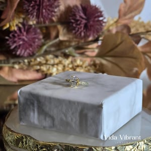 May include: A gold ring with a crescent moon design and clear cubic zirconia stones. The ring is on a white marble surface.