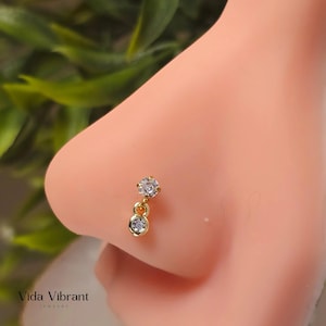 May include: Gold nose ring with two clear round cubic zirconia stones. The top stone is larger than the bottom stone.