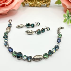 May include: A silver bracelet and earrings set with green and blue crystals. The bracelet features a silver oval charm and the earrings have a silver leaf charm.