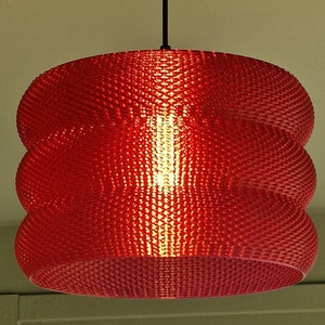 Könnte beinhalten: Eine rote Pendelleuchte mit strukturiertem, geschichtetem Design. Sie hängt an einem schwarzen Kabel und einer Deckenhalterung. Die Glühbirne ist im Inneren des Schirms sichtbar und wirft einen warmen Schein.