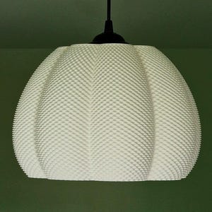 May include: White pendant light fixture with a textured, rounded shade. The light hangs from a black rod and ceiling mount. The shade has a dotted pattern. The background is a muted green.