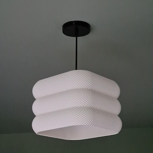 May include: White, textured pendant light with a black ceiling fitting. The lampshade has a distinctive, layered design. The light fixture is suspended from the ceiling.