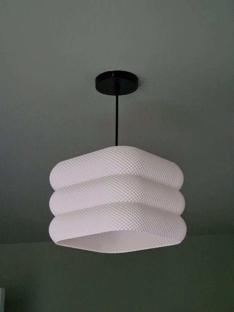May include: White, textured pendant light with a black ceiling fitting. The lampshade has a distinctive, layered design. The light fixture is suspended from the ceiling.