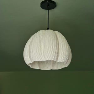 May include: A white, textured pendant light fixture with a round, dimpled shade. The light hangs from a black cord and ceiling mount. The shade has a unique, organic shape and a dotted surface.