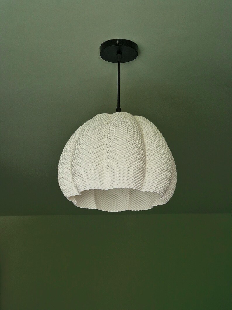 May include: A white, textured pendant light fixture with a round, dimpled shade. The light hangs from a black cord and ceiling mount. The shade has a unique, organic shape and a dotted surface.