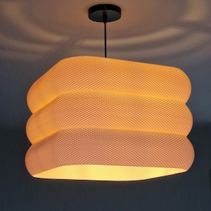 May include: A contemporary pendant light with a textured, off-white shade. The shade is square with rounded edges and is suspended from a black ceiling mount. The light emits a warm glow, perfect for a living space or dining area.