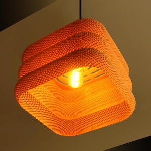 May include: Orange, textured pendant light fitting with a square shape. The light has a layered design and a visible lightbulb. The fitting is suspended from a black cord.