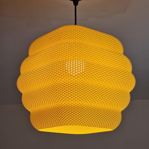 Op de afbeelding: Een felgele hanglamp met een gestructureerd, honingraatachtig oppervlak. De lamp heeft een ronde, bolvormige vorm en hangt aan het plafond met een zwart snoer en een bijpassende zwarte, ronde plafondkap.
