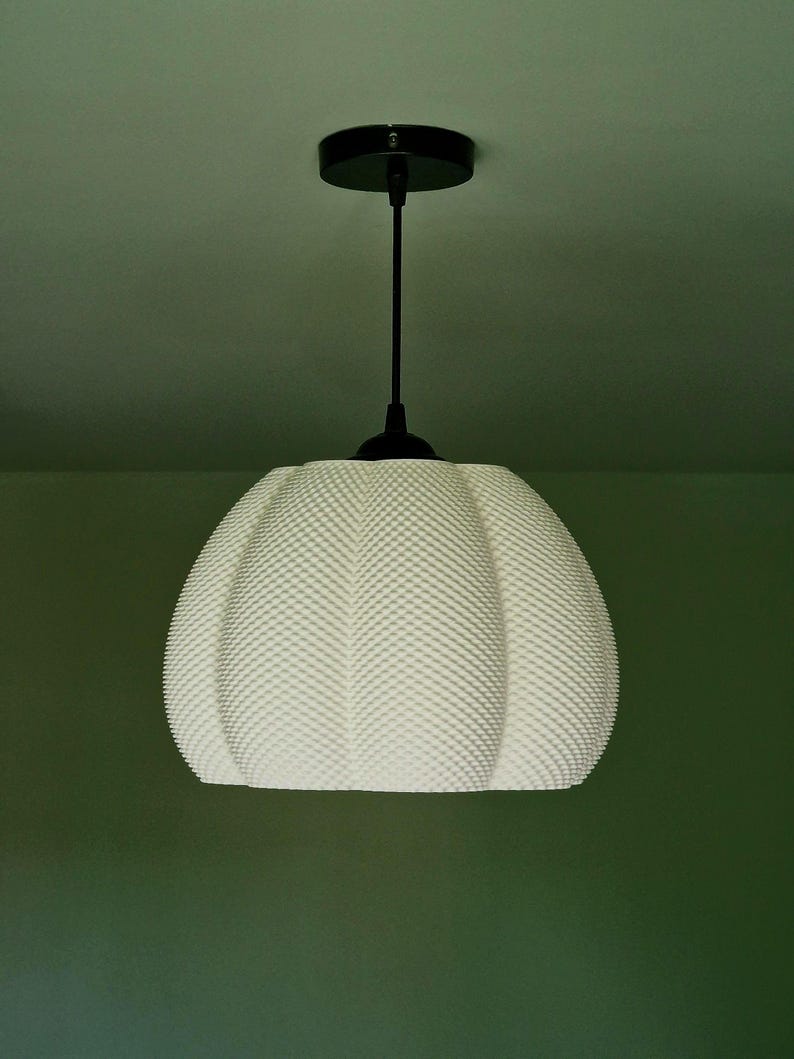 May include: White pendant light fixture with a textured, rounded shade. The light hangs from a black rod and ceiling mount. The shade has a dotted pattern. The background is a muted green.