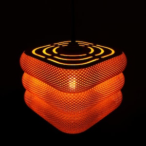 May include: An orange, textured pendant light with a unique, layered design. The light has a geometric shape with a series of concentric circles cut into the top. The light is illuminated from within, creating a warm glow against a black background.