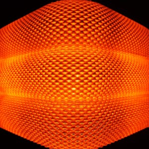 May include: A close-up of an abstract, geometric form with a honeycomb texture, glowing with an orange light. The surface is made up of small, repeating square patterns. The background is a deep black, which makes the object's orange glow stand out.