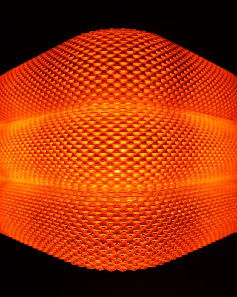 May include: A close-up of an abstract, geometric form with a honeycomb texture, glowing with an orange light. The surface is made up of small, repeating square patterns. The background is a deep black, which makes the object's orange glow stand out.