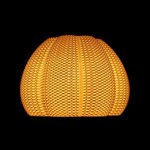 May include: A woven, dome-shaped lampshade in a warm, golden-yellow hue. The shade has a textured surface with a repeating pattern of small, rectangular openings. The background is solid black, highlighting the lampshade's shape and color.