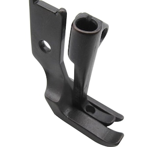 May include: A black metal sewing machine foot with a curved needle plate and a metal guide. The foot is designed for sewing thick fabrics.