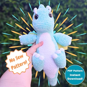May include: A light blue and white crocheted dragon plush toy with large, round eyes. The dragon has small wings and is being held up by a hand. Text on the image says "No Sew Pattern!" and "PDF Pattern Instant Download!"