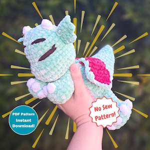 May include: A crocheted dragon plushie in shades of mint green, pink, and white. The dragon has closed eyes and a smiling expression. The image includes text that says "PDF Pattern Instant Download!" and "No Sew Pattern!"