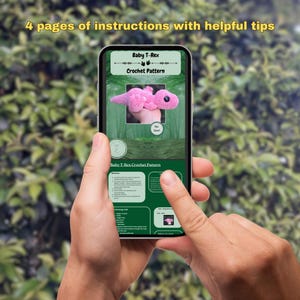 Pu&ograve; includere: Uno smartphone che mostra uno schema di uncinetto per un bambino T-Rex rosa. Lo schema include istruzioni e suggerimenti utili. Il testo sullo schermo recita "Baby T-Rex Crochet Pattern".