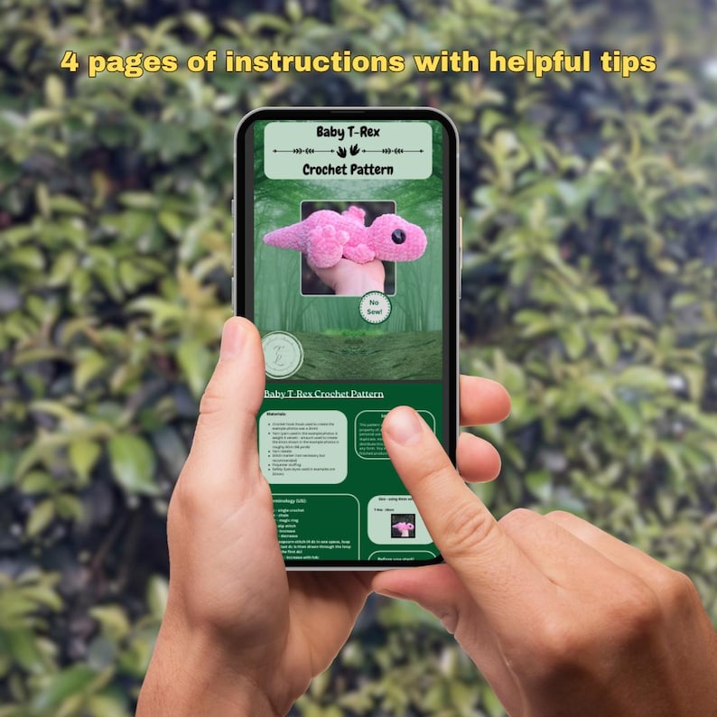 Pu&ograve; includere: Uno smartphone che mostra uno schema di uncinetto per un bambino T-Rex rosa. Lo schema include istruzioni e suggerimenti utili. Il testo sullo schermo recita "Baby T-Rex Crochet Pattern".