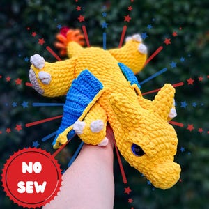 May include: A handmade yellow and blue crochet dragon toy with blue eyes and white accents. The dragon has blue wings and a flame-like tail. The image has a red and blue starburst design and the text "NO SEW" in a red circle.
