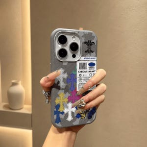 May include: A grey smartphone case featuring a repeating pattern of multi-colored crosses in white, yellow, blue, and pink. The case includes a rectangular white label with the text CHROME HEART, a barcode, and various small graphic symbols.
