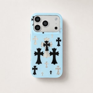 Puede incluir: Una funda de smartphone de color azul claro con un patrón disperso de emblemas de cruz en negro y tono plateado. La funda tiene un recorte rectangular en la parte superior para un sistema de triple cámara y flash, con un acabado liso y brillante.