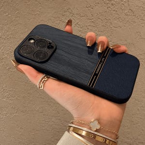 Puede incluir: Una funda de smartphone azul oscuro con textura de veta de madera en el lado izquierdo y un patrón de rayas cruzadas en el derecho. Una fina franja vertical dorada separa ambas secciones, con el texto WONDERFUL LIFE impreso en letras doradas.