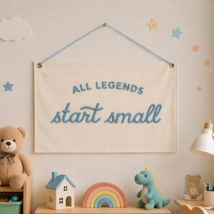 May include: A children's room scene with a wooden bookshelf, toys, and wall decorations. The wall features a banner with the text "ALL LEGENDS start small". Toys include a teddy bear, a dinosaur, a rainbow, and a house.
