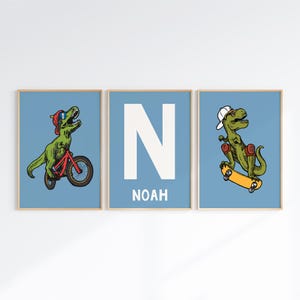 May include: Three blue and white prints with a dinosaur riding a bike, a dinosaur skateboarding, and a large white letter N with the name Noah below it.