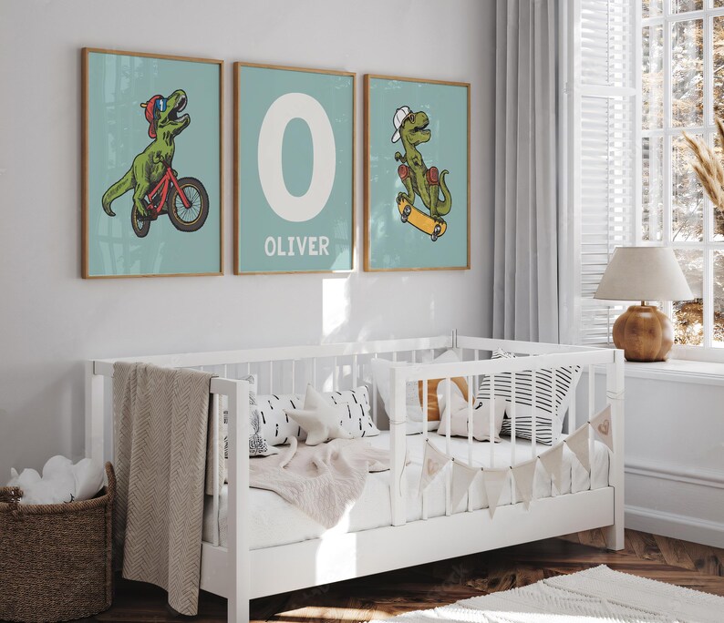 May include: Three framed prints with a light blue background. The prints feature a green dinosaur riding a bicycle, the letter O, and a green dinosaur riding a skateboard. The letter O print has the name Oliver written below it.