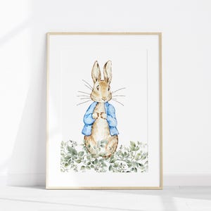 May include: Watercolor illustration of a rabbit wearing a blue jacket, set against a white background. The framed artwork features the rabbit standing amidst green foliage. The artwork is in a light wooden frame.