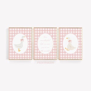 May include: Set of three framed prints featuring a charming goose illustration. Each print has a pink gingham background and a gold frame. One print has the text "How wonderful life is now you're in the world."