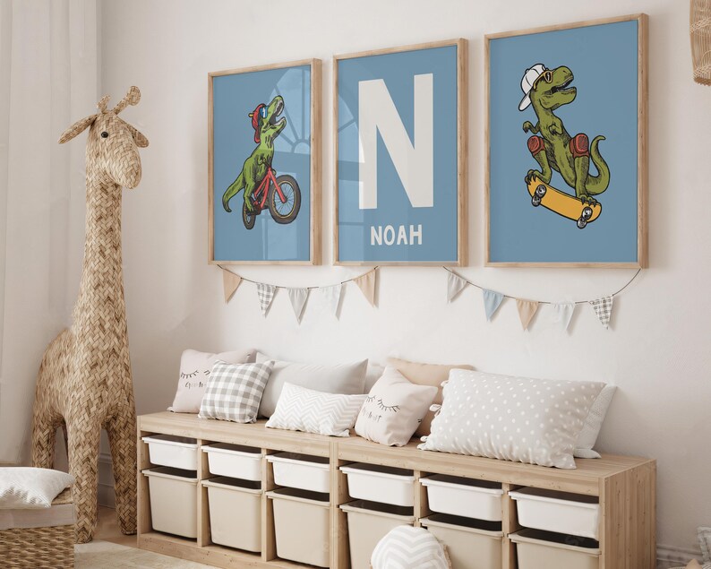 May include: Three framed prints with a blue background. The prints feature a dinosaur riding a skateboard, a dinosaur riding a bicycle, and the letter N with the name Noah underneath.