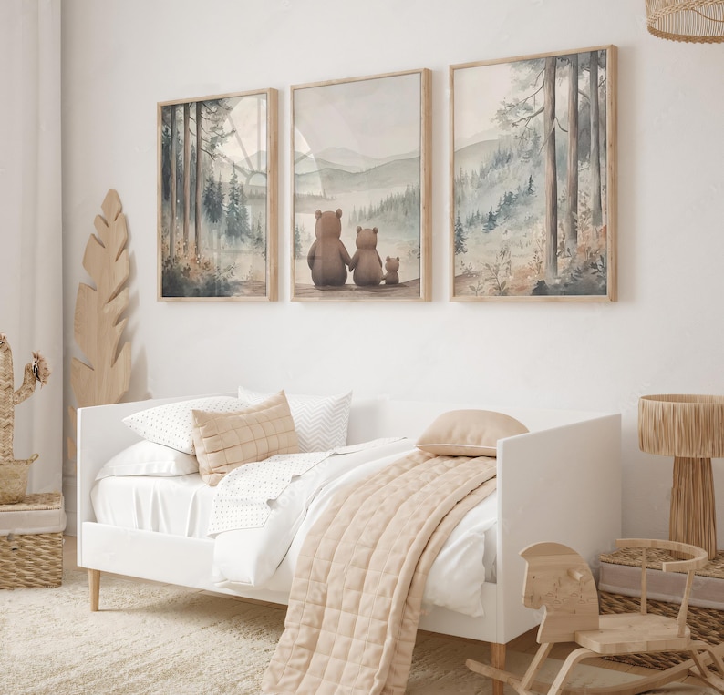 May include: Three framed watercolour prints showing forest scenes and a bear family. The prints are above a white bed with beige bedding and pillows. A wooden rocking horse and a woven basket are also visible.