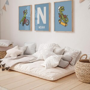 May include: Three framed prints with a blue background. The prints feature a dinosaur riding a bicycle, the letter N with the name Noah below it, and a dinosaur riding a skateboard.