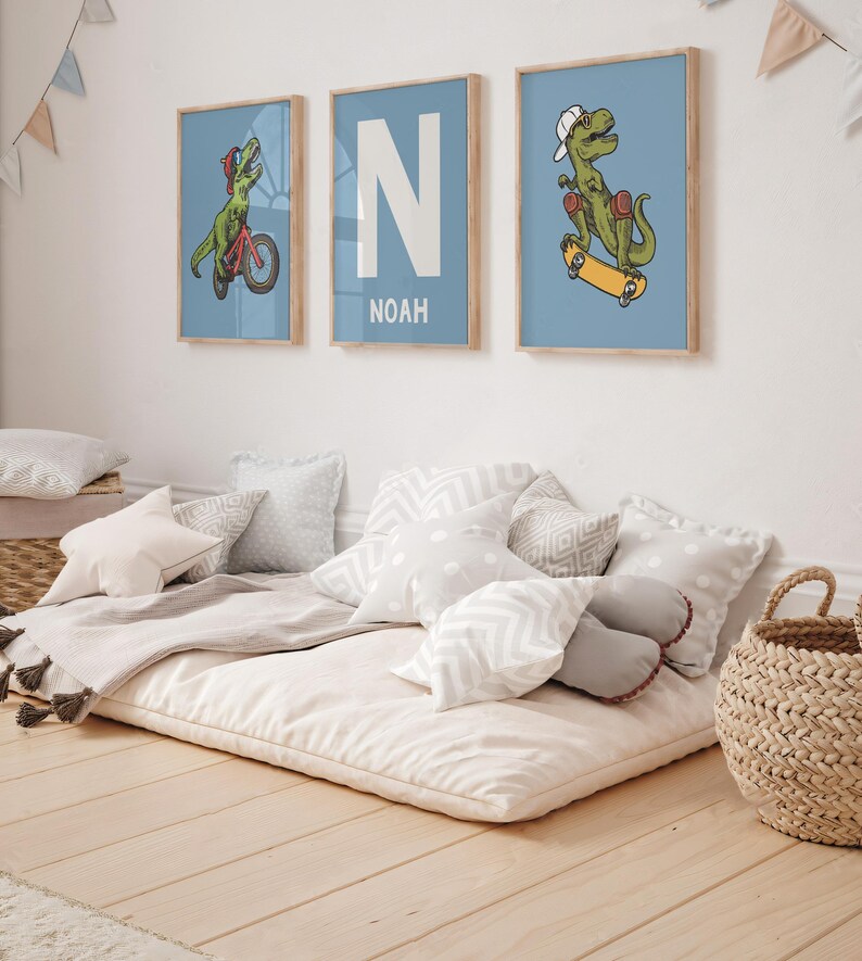 May include: Three framed prints with a blue background. The prints feature a dinosaur riding a bicycle, the letter N with the name Noah below it, and a dinosaur riding a skateboard.