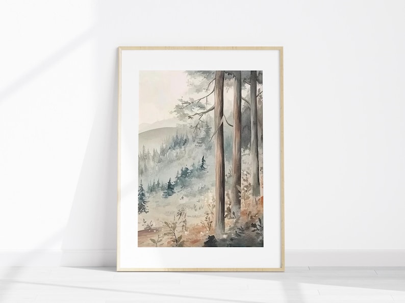 May include: Watercolour painting of a forest scene in a wooden frame. The artwork depicts tall trees in the foreground with a misty mountain landscape in the background. The colour palette includes shades of grey, brown, and green.