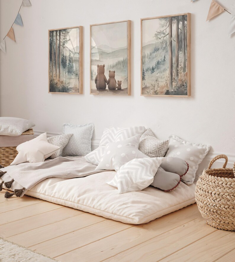 May include: Three framed watercolour prints of a forest scene and a family of bears hang above a floor cushion with pillows. The pillows are various shapes and patterns in shades of white and grey. A woven basket sits nearby.
